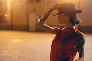 The young, attractive girl in a hat poses to the camera at night photo