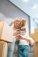 Young happy family with kid unpacking boxes together sitting on sofa photo