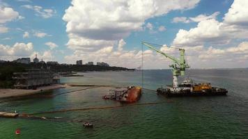 navio de resgate com guindaste levantando navio de carga destruído no porto de odessa video