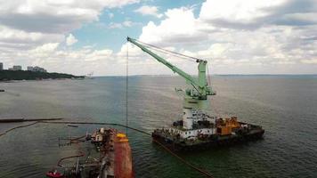 Rescue ship with crane lifting wrecked cargo ship at port in Odessa video
