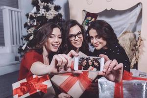 Beautiful girl photographed themselves on the phone on the background of Christmas gifts. Decorative vintage apartment. photo