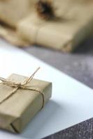 regalos de vacaciones caja de regalo de navidad y año nuevo envuelto en papel marrón, conos de pino y papel blanco y bolígrafos colocados sobre la mesa, copie el espacio. foto