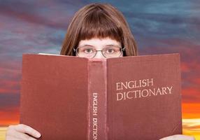 la chica mira el diccionario de inglés y el cielo del atardecer foto
