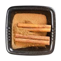 cinnamon sticks and powder in black bowl isolated photo