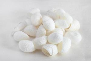 many organic silkworm cocoons on white silk fabric photo