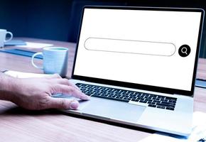 Businessman hand pressing keyboard laptop with icon search engines on display laptop and coffee cup on table photo