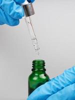 hand hold pipette with medicine oil in a bottle on gray background photo