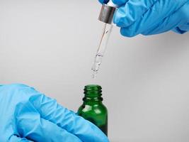 a doctor in gloves holds a pipette and a bottle of medicine in his hands photo