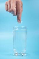 hand puts a pill in a glass on a blue background, headache treatment photo