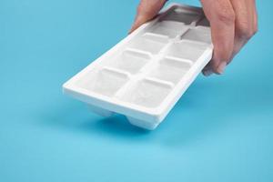 caja con cubitos de hielo en la mano sobre un fondo azul foto