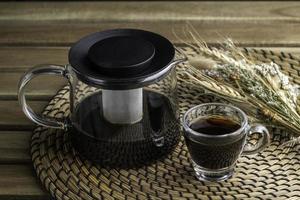 A cup of black coffee is poured into a small empty cup on a wooden table. photo