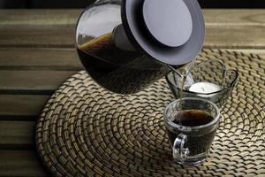 Black coffee is being poured into a small clear cup on a wooden table. photo