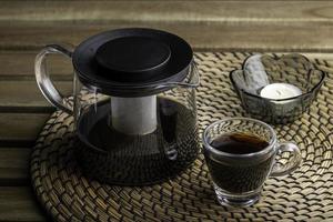 se vierte una taza de café negro en una pequeña taza vacía sobre una mesa de madera. Para el desayuno foto