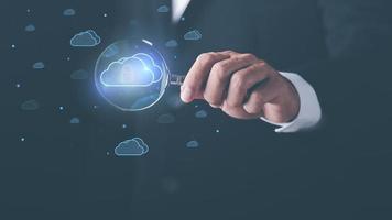 businessman holding a magnifying glass shows the use of cloud network technology to communicate and connect data servers around the world. with the innovation of online internet from virtual screen photo