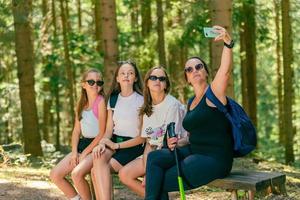 Mountaineers take selfie with phone on a wooden bench. Forest in background photo