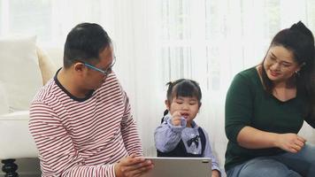 feliz familia asiática en casa de vacaciones los padres están enseñando a sus hijas a mirar tabletas y cantar. danza feliz video