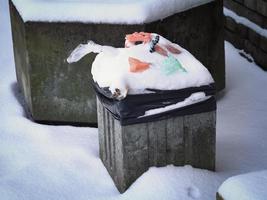 Concrete waste bin filled with trash standing on a sidewalk covered in snow photo