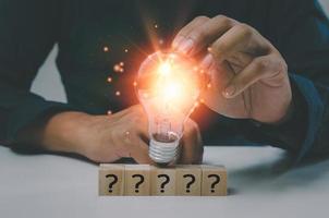 Creative success idea inspiration business concept innovation solution On the desk is a hand holding a light bulb and a wood cube block question mark text icon. photo