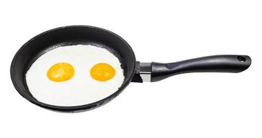 two fried eggs in black frying pan isolated photo