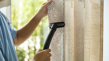 man dry cleaning curtain with vacuum cleaner. in living room at home. photo