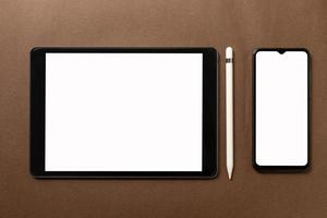 Black tablet with white blank screen is on top of brown paper with supplies. Top view, flat lay. photo