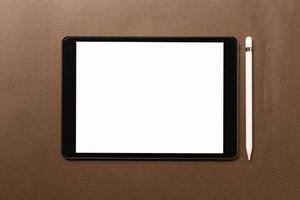 Black tablet with white blank screen is on top of brown paper with supplies. Top view, flat lay. photo