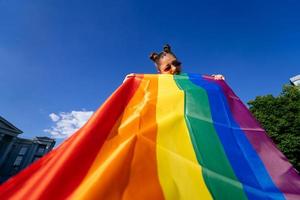 una mujer joven desarrolla una bandera del arco iris contra el cielo foto
