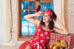 hermosa mujer en pijama con caja de regalo, ventana en el fondo. foto