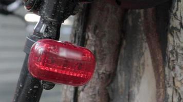 vélo rouge clignotant led feu arrière. l'arrière d'un vélo garé près d'un arbre avec des images de lumière rouge clignotante. clignotant de vélo en action. video