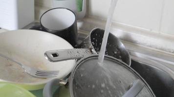 die Küchenutensilien im Waschbecken müssen gewaschen werden. ein Haufen schmutziges Geschirr in der Küchenspüle mit fließendem Wasser. Küchenutensilien müssen gewaschen werden. Hausaufgabenkonzept. video