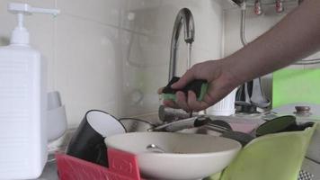 la mano aprieta una esponja con espuma. la mano de un hombre presiona el dispensador y saca detergente líquido en una esponja verde para lavar platos sucios y grasientos, de cerca. Rutina típica de cocina. video