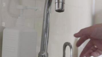 a mão de um homem abre a torneira, aperta o dispenser e puxa o detergente líquido para uma esponja verde, apertando-a. lavando pratos sujos e gordurosos, close-up. rotina típica da cozinha. video