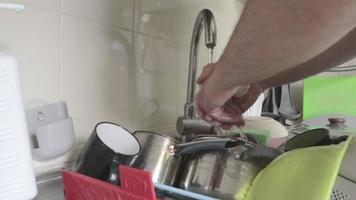 avvicinamento di il cucina Lavello svolta via il acqua. Uomini mani lavato un' lotto di piatti con un' verde spugna e trasformato via il rubinetto. spray. caduta gocce di acqua. chiudere. video