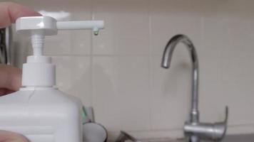 A man's hand presses a dishwashing liquid soap dispenser on a dirty sink full of dishes and kitchen utensils. Washing dishes in the kitchen by hand with detergent and sponge. video