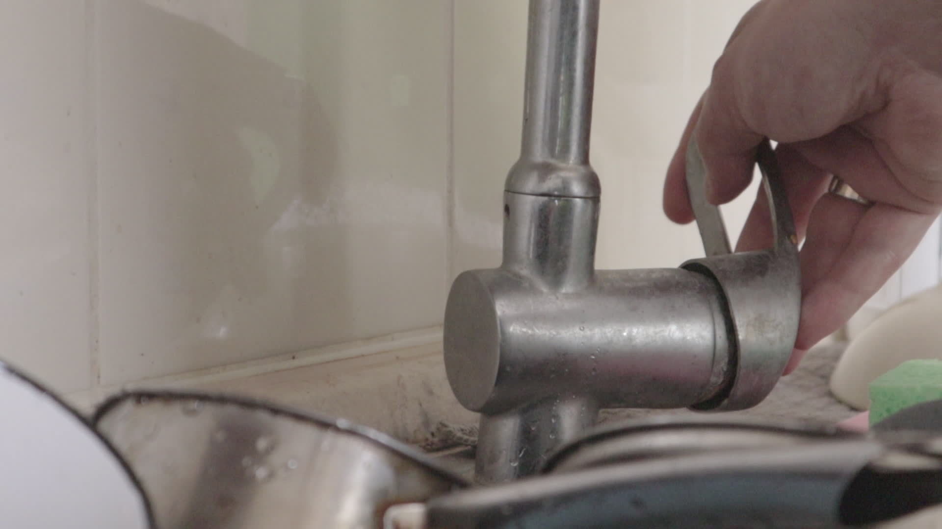 A man's hand opens a water faucet before washing dishes in the kitchen