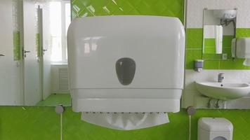 dispensador de toallas de papel en la pared. pañuelos blancos en una caja de plástico blanca en un baño público. saque un trozo de papel para limpiarse las manos y la cara mojadas. el concepto de atención médica y prevención. video