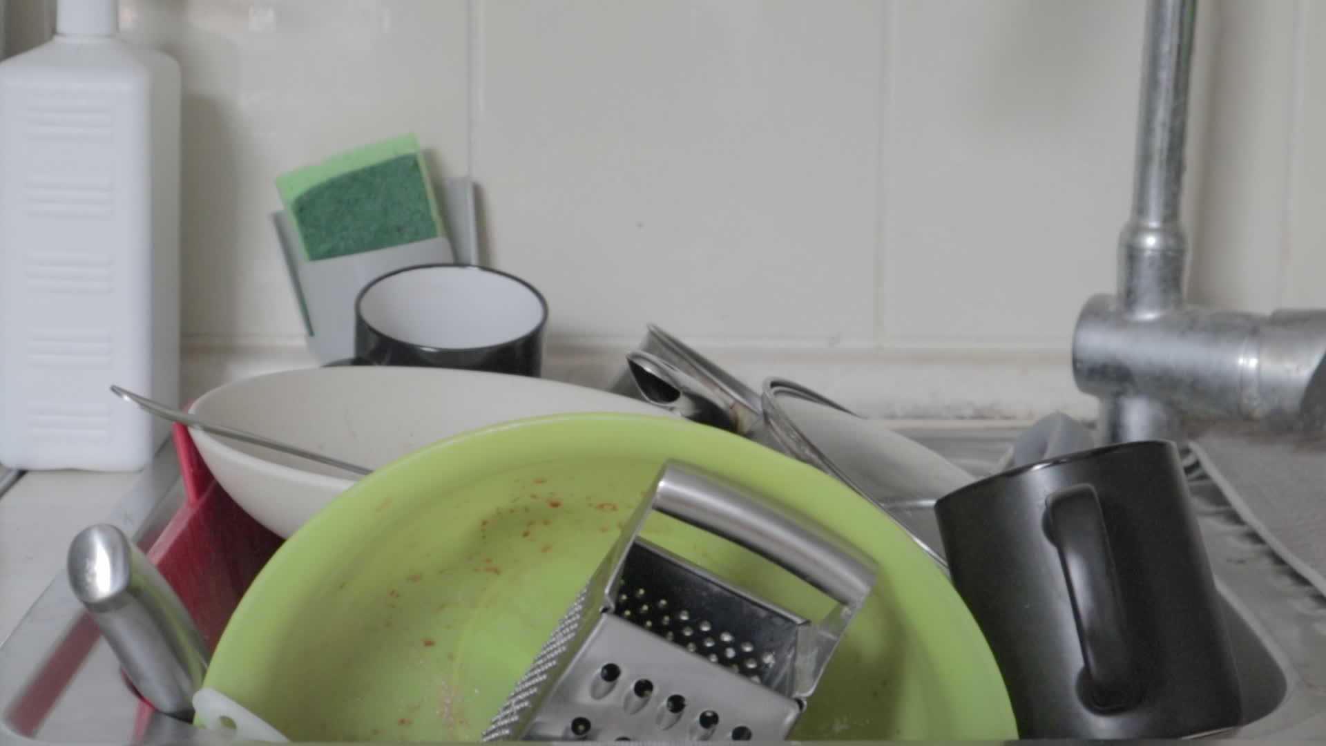 The kitchen utensils in the wash basin need to be washed. A pile of