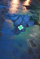 green cross of drugstore reflected in rain puddle photo