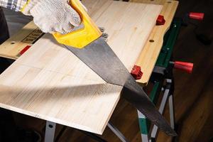 woodworker saws wooden board with hand saw photo