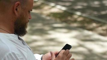 A man in a white shirt in the park on the same lake looks at a smartphone video