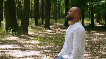 um homem com barba em uma camisa branca medita no parque video