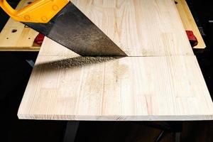 side view of hand saw sawing solid wooden board photo