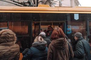 Many unidentified people are waiting for city transport at the bus stop photo