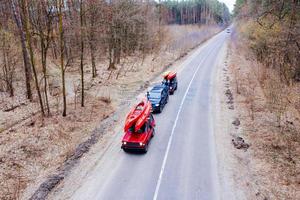 Several cars with kayaks on roof rack driving on the road among trees photo