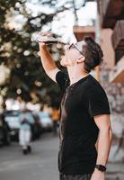 joven hipster atractivo en la calle bebe una bebida fría en un día de verano. foto