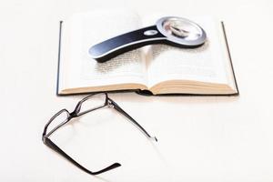eyeglasses and magnifier on open book on table photo