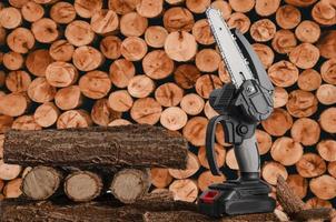 Light chain saw with battery on a pile of sawn tree trunks in the garden. photo