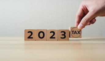 Holding a wooden block with tax 2023. Concept of planning to pay taxes in 2023. paying the tax rate. Taxation, taxes burden. photo