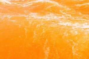 Defocus blurred transparent orange colored clear calm water surface texture with splash, bubble. Shining orange water ripple background. Surface of water in swimming pool. Orange bubble water, splash. photo