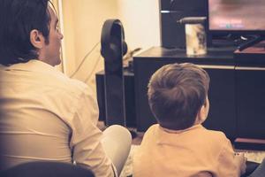 Rear view of father and son playing video games at home. photo